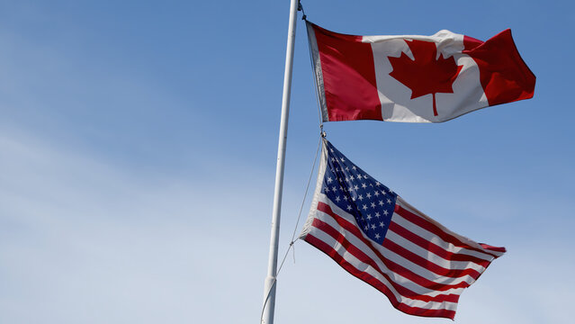 canada and usa flags fluttering in the wind on blue sky copy space blue sky background