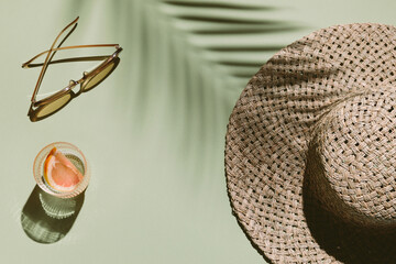 Summer flat lay with straw hat, sunglasses and glass of water with grapefruit slices on green...