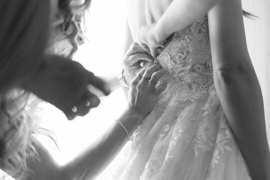 foto in bianco e nero del dettaglio di mani che si accingono a chiudere i bottoni di un abito appena indossato da una sposa 
