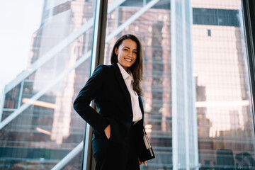 Cheerful businesswoman standing against window during break from work