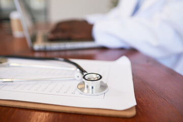 Close up of doctor's stethoscope while Black doctor uses laptop in background
