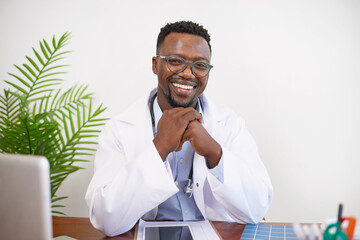 Portrait of a Black GP doctor sitting at his desk writing and smiling