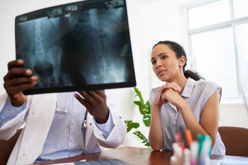 Fototapeta na wymiar Black male doctor explains x-ray results to young worried patient in office