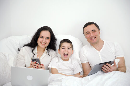 Happy family and digital technology. family parents and son lying on bed using smart phones success winning.