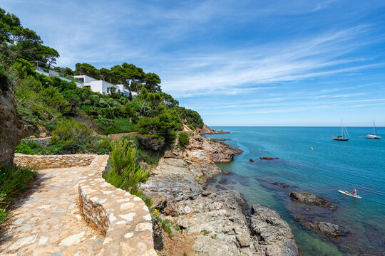 Coastal path along the cliff with view to sea, anchored yachts and padling couple - June 2018 - Sa Riera, Costa Brava, Catalonia, Spain