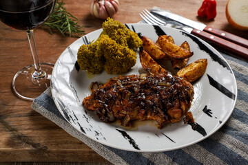 grilled chicken fillet with onion sauce accompanied by roasted potatoes and cooked broccoli with a glass of wine and garlic on the side