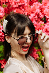 A brunette in a beige dress and glasses among blooming azaleas