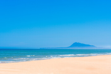 A beach with a blue sky and a mountain in the background