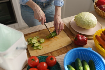 Female hands cutting cucumbers with a knife on a kitchen table. Woman cooking healthy vegetarian...