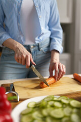 Woman cuts carrot for salad on a wooden cutting board. Female person cooking healthy vegetarian meal in a domestic kitchen