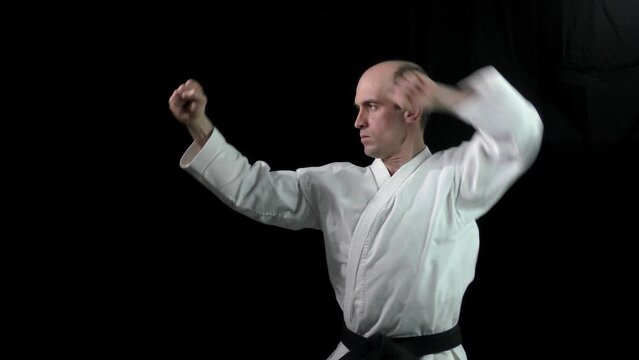 On a black background, an adult athlete performs formal karate exercises