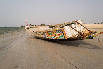 une pirogue peinte échouée sur la plage au Sénégal en Afrique - obrazy, fototapety, plakaty