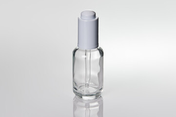 Glass white transparent dropper bottle. Close-up, photo on a reflective surface.