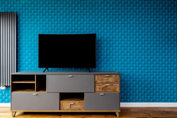 A wall with blue patterned wallpaper. A dresser with drawers and a large flat-screen TV. Plenty of...