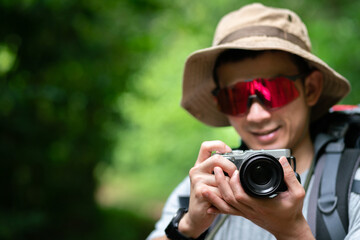 happy asian photographer travel and take photo with digital camera and backpacker trail trekking in nature forest on high mountain, hobby activity in weekend