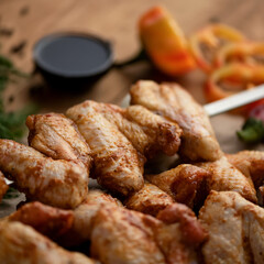 Chicken wings shish kebab. Chicken wings on skewers. Wooden table with sauce and vegetables. Close-up. Wooden background. Top view. 