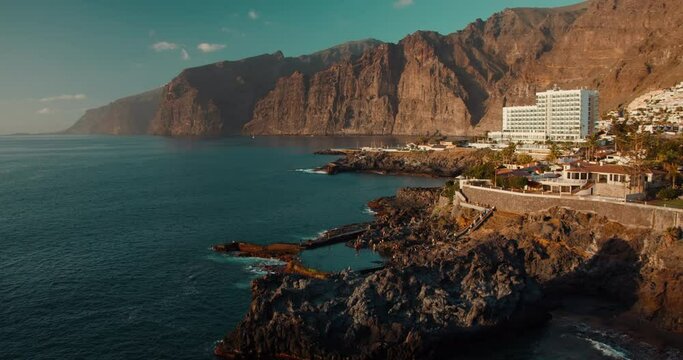 Natural ocean swimming pool in Tenerife Canary Islands. Charco de Isla Cangrejo. Gorgeous view to the Los Gigantes cliffs at sunset orange light.