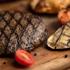 Grilled steak with vegetables on wooden board. Piece of fried meat on table with tomato, eggplant. Barbecue menu. View from above. Close-up. soft focus.