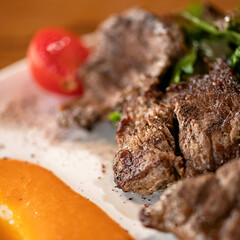 Grilled pieces of meat with spinach garnish, sauce and cherry tomatoes on white plate. Grilled pork. View from above. Close-up.Soft focus. 