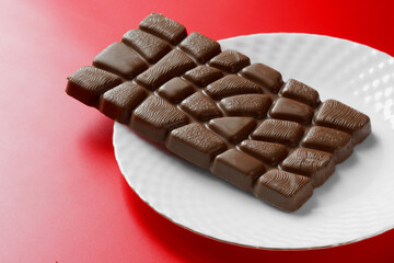 Whole rectangular bar of chocolate in a white plate on a bright red background.