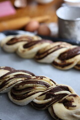 braid with chocolate, raw dough for a bun with chocolate. Freshly baked chocolate swirl pastry - babka. Baker make buns from dough with poppy and chocolate filling. Cooking twisted pie. Top view