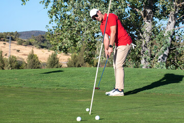 Golfer putting ball in the practice hole. Golf on the driving range shooting several golf balls at the flag. Golfer practicing his putt looking at the ball after the shot
