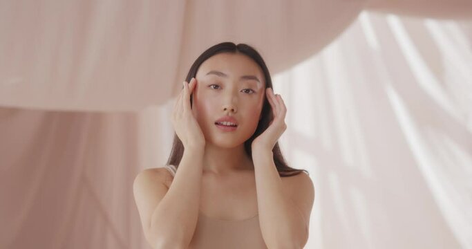 Attractive Asian woman posing to camera. Pretty girl having healthy, soft skin after cosmetic product. Hand touching beauty, smooth and elastic face. Perfect skin. Dermatology concept.