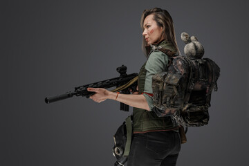 Studio shot of attacking female mercenary with backpack and rifle.