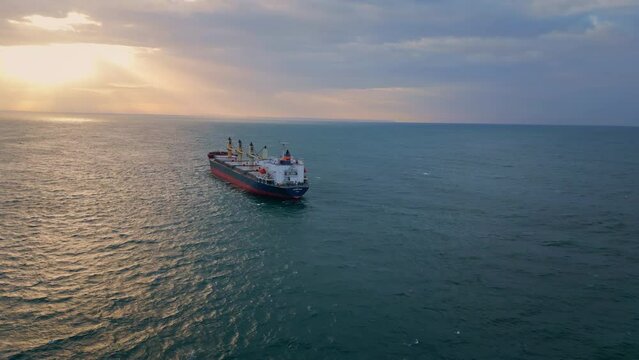 Bulk carrier ship sailing to sunset. Drone view vessel floating in dark ocean.