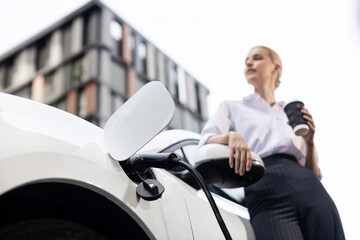 Progressive businesswoman with electric car and charging station before driving around city center....
