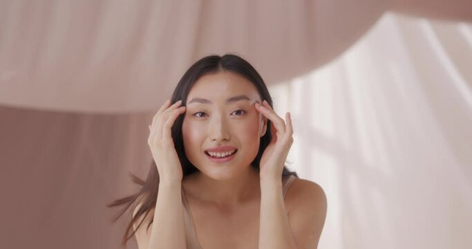 Pretty young Asian woman regularly doing massage for her face every morning. Happy female smiling and touching, patting beautiful face. Skin looking elastic, toned and healthy. Face massage concept.