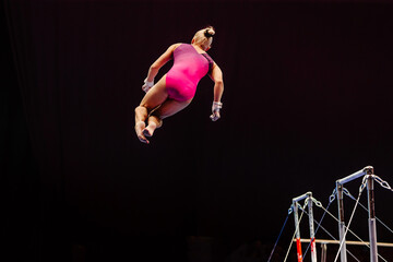 female gymnast performing somersault gymnastics on uneven bars, black background, sports summer...