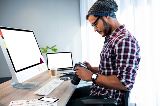 Man looking at digital camera while sitting by computer