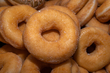 Many sweet and tasty round doughnuts, ring donuts covered with sugar. Chocolate-frosted doughnut. Symbol of sweeties, fried dough. A lot of sweet unhealthy food. Food waste, food production.