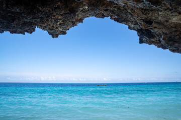 View of the Indian Ocean from Zanzibar Tanzania, with a small boat on the water, sea cave rock formations in foreground