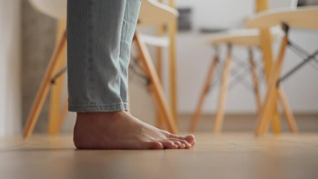 A barefoot girl with bare feet walks on a wooden floor in her apartment at home, Morning light girl makes steps with her bare feet, Foot movements dressed in blue jeans. Walking on a wooden floor
