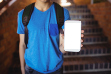 Schoolboy standing with schoolbag showing mobile phone near staircase at school