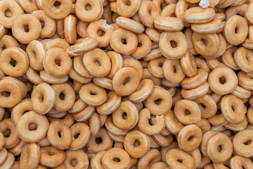 Many sweet and tasty round doughnuts, ring donuts covered with sugar. Chocolate-frosted doughnut. Symbol of sweeties, fried dough. A lot of sweet unhealthy food. Food waste, food production.