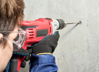 A guy is drilling a hole in the wall with an electric drill