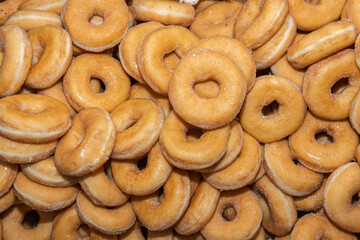 Many sweet and tasty round doughnuts, ring donuts covered with sugar. Chocolate-frosted doughnut. Symbol of sweeties, fried dough. A lot of sweet unhealthy food. Food waste, food production.