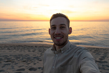 young man in a shirt, taking a selfie in a sunset on the beach