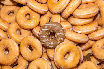 Many sweet and tasty round doughnuts, ring donuts covered with sugar. Chocolate-frosted doughnut. Symbol of sweeties, fried dough. A lot of sweet unhealthy food. Food waste, food production.