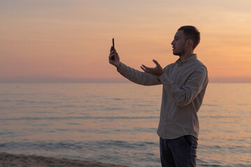 young man in shirt using cell phone on the beach with sunset