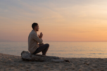 young man in a shirt, making a prayer in a sunset on the beach
