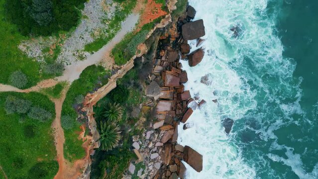 Drone view coastal cliffs covered green grass bushes. Waves washing shore stones