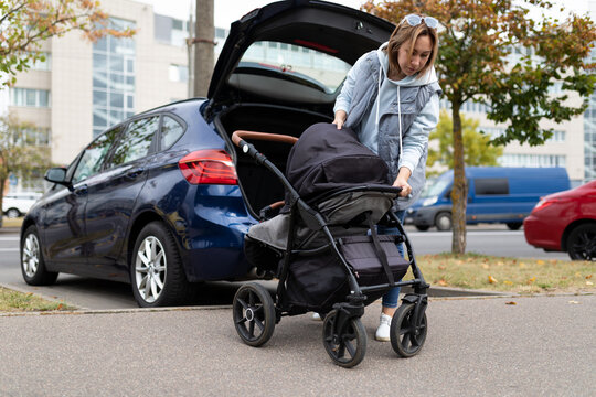 young woman parent folds the baby stroller into the luggage compartment of the car