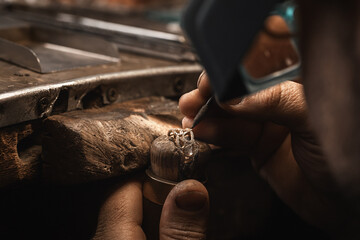 Close up of a goldsmith's hand making a gold or silver ring or a diamond using goldsmith's tools. Making ring with diamonds - obrazy, fototapety, plakaty