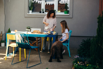 Mother is pouring milk for breakfast and daughter pats a dog in the backyard