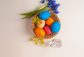 in a small basket are multi-colored painted eggs. flowers lie nearby. Top view