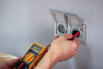 Male Electrician Checking Voltage Of Socket With Multimeter